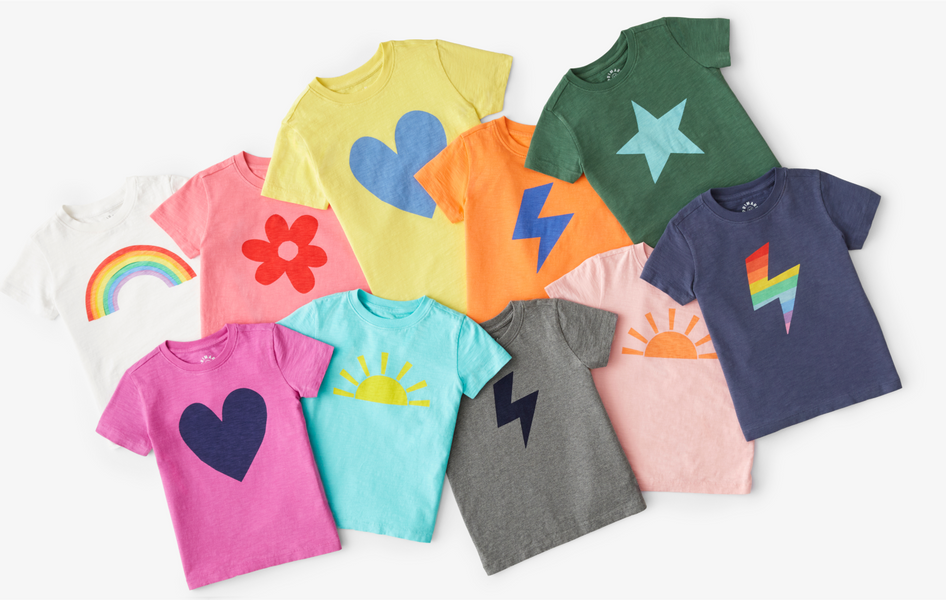 10 different kids t-shirts in arainbow of colors, with graphics on them, including hearts, rainbows, lightning bolts and stars.