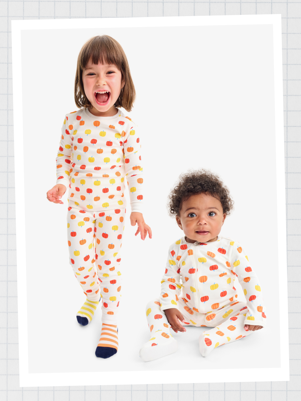 A kid and baby next to each other wearing matching pumpkin PJs