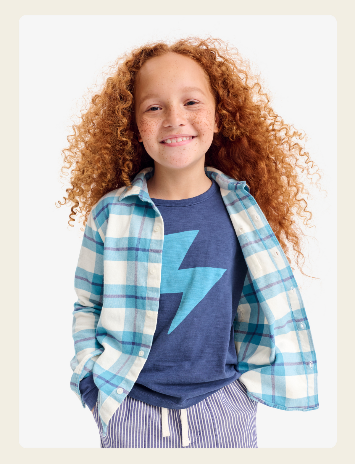 A kid standing up looking at the camera wearing a bolt tee with a flannel over it.