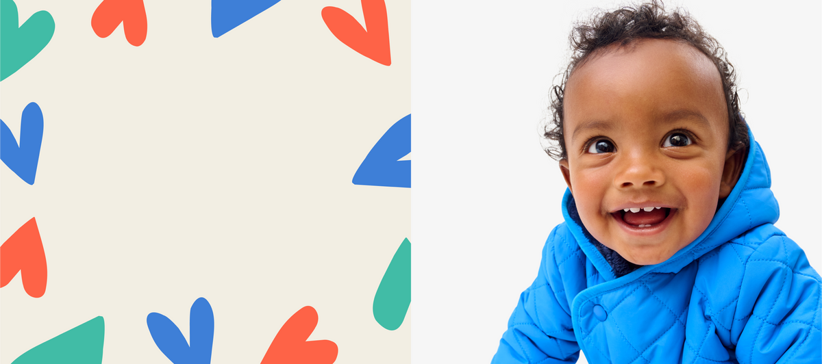 A young baby smiling at the camera wearing a blue quilted puffer jacket.