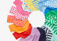 A laydown of our one-piece swim rash guards in rainbow order.